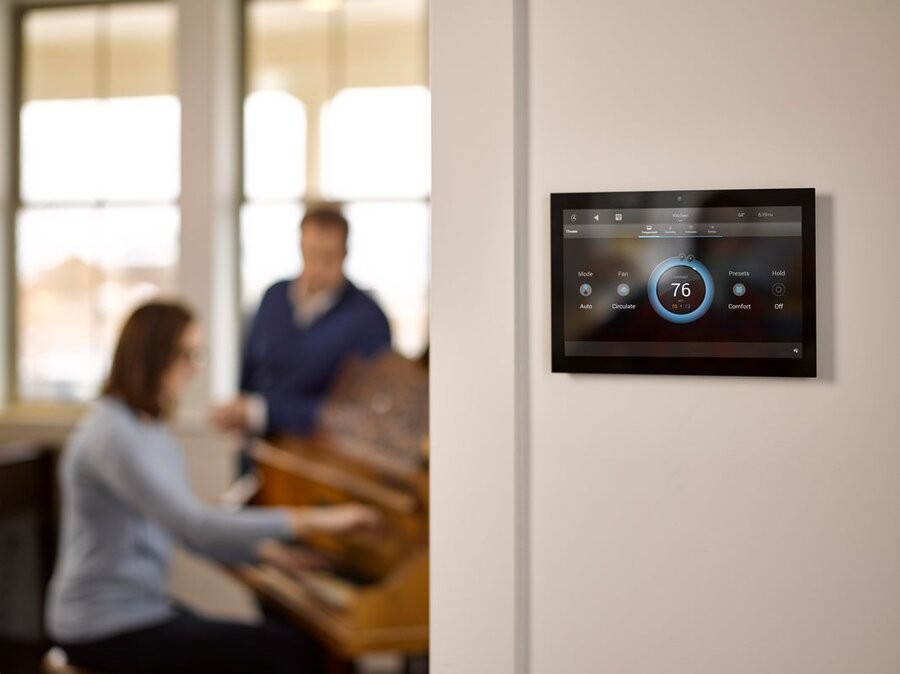 A hallway outside a room featuring a wall touchscreen with a Control4 interface.
